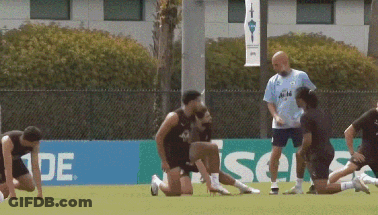 A Group Of Soccer Players Are Stretching On A Field In Front Of A Sign That Says ' Ade ' GIF