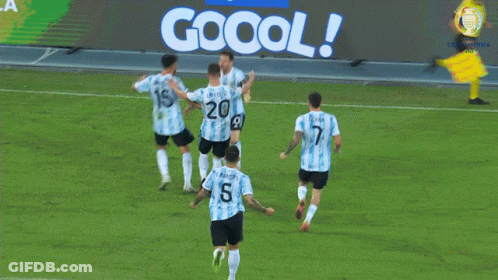 A Group Of Soccer Players Celebrate A Goal In Front Of A Jogo Oficial Sign GIF
