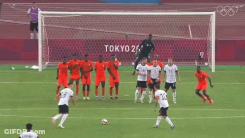 A Group Of Soccer Players On A Field With Tokyo 2020 Written On The Wall Behind Them GIF