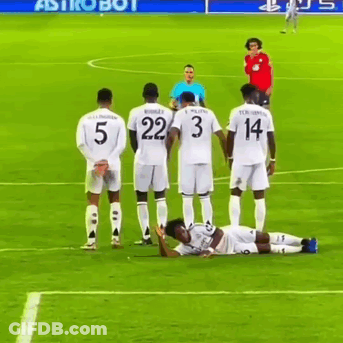 A Group Of Soccer Players Standing Around A Player Laying On The Field GIF