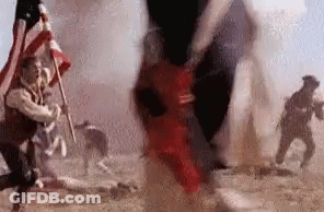 A Group Of Soldiers Are Fighting In A Field While A Man Holds An American Flag . GIF