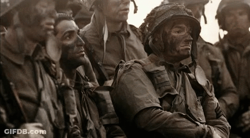 A Group Of Soldiers Are Sitting In A Line And One Of Them Has A Helmet On GIF