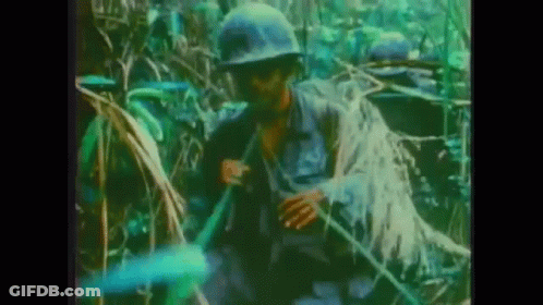 A Group Of Soldiers Are Standing In The Jungle Holding A Rifle . GIF