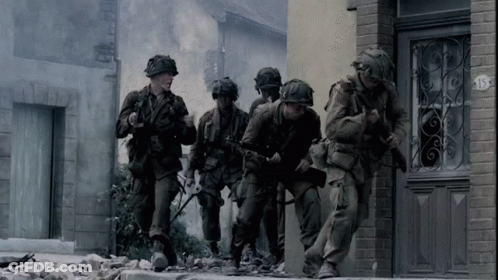 A Group Of Soldiers Are Walking Down A Street In Front Of A Building With The Number 15 On It GIF