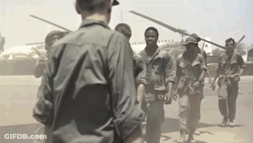 A Group Of Soldiers Are Walking In Front Of A Helicopter GIF