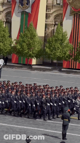 A Group Of Soldiers March Down A Street In Front Of A Building GIF