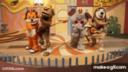 A Group Of Stuffed Animals Are Standing On A Stage With Dominoes In The Background GIF