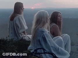 A Group Of Three Women Are Sitting On Top Of A Hill Looking At The Sunset . GIF