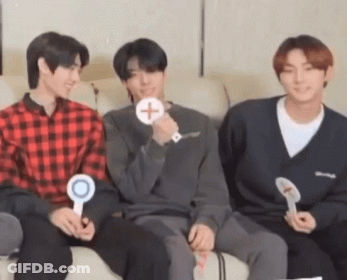 A Group Of Three Young Men Are Sitting On A Couch Holding Signs . GIF