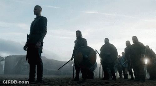 A Group Of Vikings Are Standing On A Beach With Shields And Swords GIF