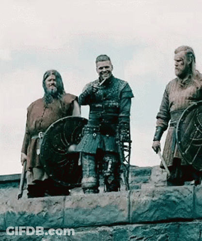 A Group Of Vikings Are Standing On Top Of A Stone Wall Holding Shields . GIF