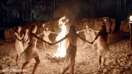 A Group Of Women Are Dancing Around A Fire On The Beach GIF