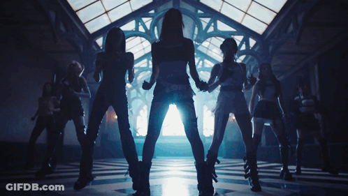 A Group Of Women Are Dancing In A Dark Room With A Light Shining Through The Windows GIF