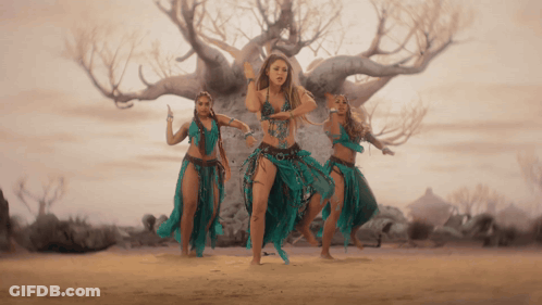 A Group Of Women Are Dancing In Front Of A Tree In The Desert GIF