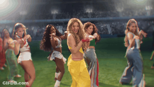 A Group Of Women Are Dancing On A Field With One Wearing A Yellow Outfit GIF