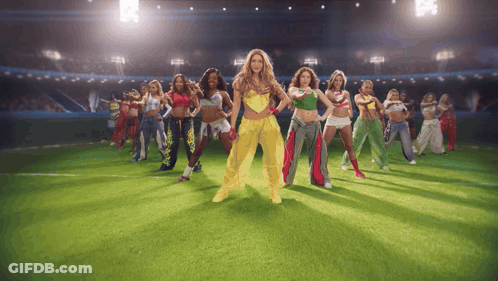 A Group Of Women Are Dancing On A Field With One Wearing A Yellow Outfit GIF