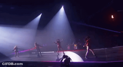 A Group Of Women Are Dancing On A Stage In A Dark Room With Purple Lights . GIF