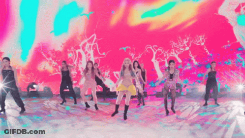 A Group Of Women Are Dancing On A Stage With A Colorful Background . GIF