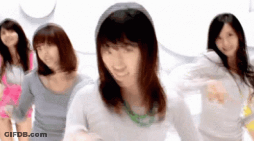 A Group Of Women Are Dancing Together In A Room And One Of Them Is Wearing A Green Necklace . GIF