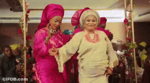 A Group Of Women Are Dancing Together In A Room With Flowers . GIF