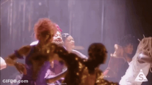 A Group Of Women Are Dancing Together On A Stage In A Dark Room . GIF