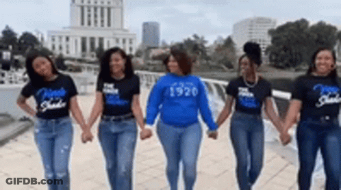 A Group Of Women Are Holding Hands In Front Of A Building . GIF