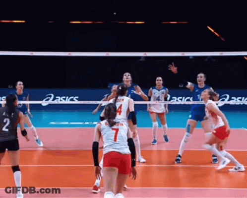 A Group Of Women Are Playing Volleyball On A Court With Asics Signs In The Background . GIF