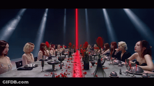 A Group Of Women Are Sitting At A Long Table With A Red Light Behind Them GIF