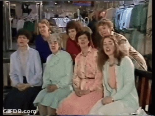 A Group Of Women Are Sitting In Front Of A Clothing Rack GIF