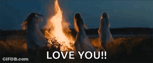 A Group Of Women Are Standing Around A Fire In A Field . GIF
