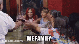 A Group Of Women Are Toasting With Wine Glasses At A Table With The Words `` We Family '' . GIF