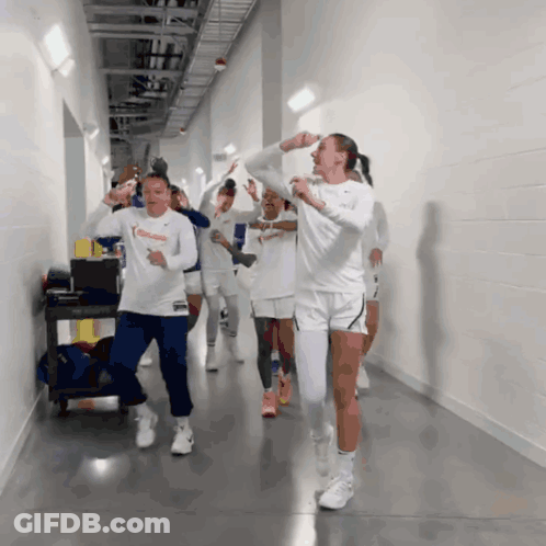 A Group Of Women Are Walking Down A Hallway And One Of Them Is Wearing A White Nike Shirt GIF