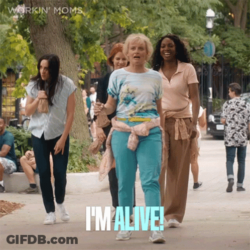 A Group Of Women Are Walking Down A Sidewalk And One Of Them Is Saying I 'M Alive GIF