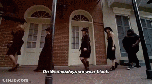 A Group Of Women Are Walking Down A Street And One Of Them Is Saying On Wednesdays We Wear Black GIF