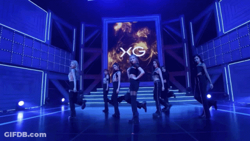 A Group Of Women Dancing In Front Of A Screen That Says Xg On It GIF