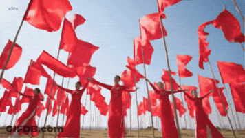 A Group Of Women In Red Dresses Are Holding Red Flags GIF