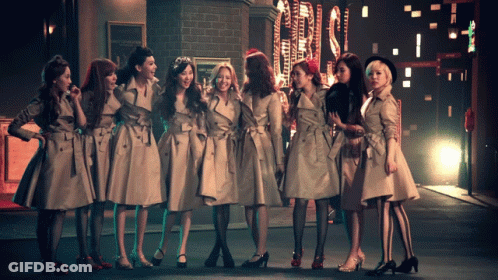 A Group Of Women In Trench Coats Are Standing In A Row GIF