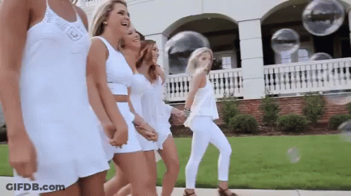 A Group Of Women In White Dresses Are Walking Down The Street . GIF