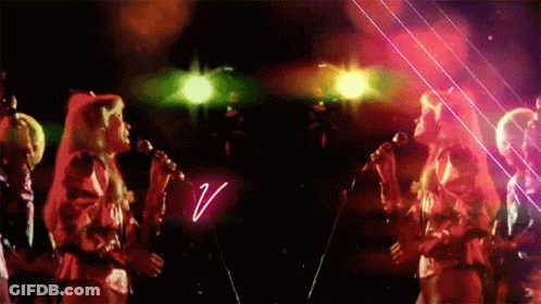 A Group Of Women Singing In Front Of A Neon Sign That Says V. GIF