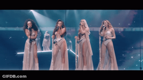 A Group Of Women Singing Into Microphones On A Stage With Angels In The Background GIF