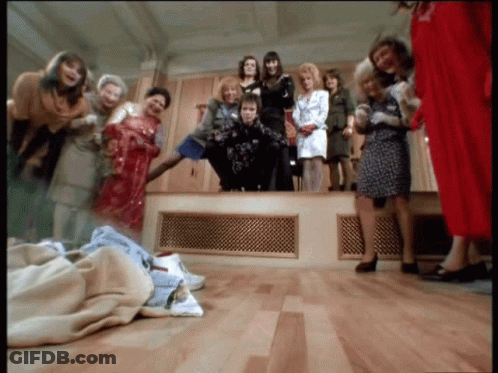 A Group Of Women Standing Around A Man In A Room GIF