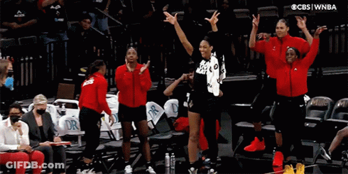 A Group Of Women Standing On A Basketball Court With Their Arms In The Air GIF