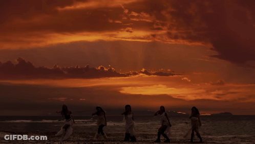 A Group Of Women Standing On A Beach At Sunset GIF