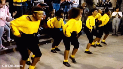 A Group Of Women Wearing Yellow Shirts And Black Pants Are Dancing In Front Of A Crowd GIF
