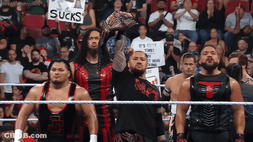 A Group Of Wrestlers Are Holding Up A Sign That Says Sucks GIF