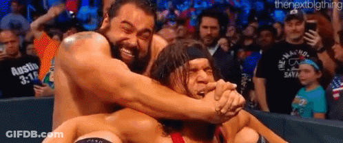 A Group Of Wrestlers Are Hugging Each Other On A Wrestling Ring In Front Of A Crowd . GIF