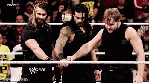 A Group Of Wrestlers Are Standing In A Ring Holding Hands . GIF