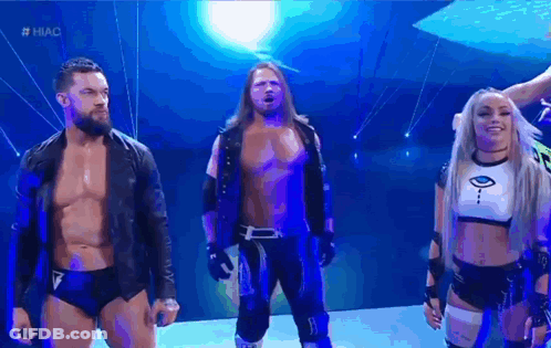 A Group Of Wrestlers Are Standing Next To Each Other On A Stage In Front Of A Blue Background . GIF