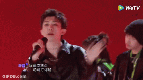 A Group Of Young Men Are Dancing And Singing In Front Of A Red Background With A Wetv Logo In The Corner GIF