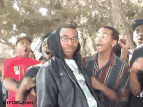 A Group Of Young Men Are Dancing In A Park And One Of Them Is Wearing A Hooded Jacket . GIF